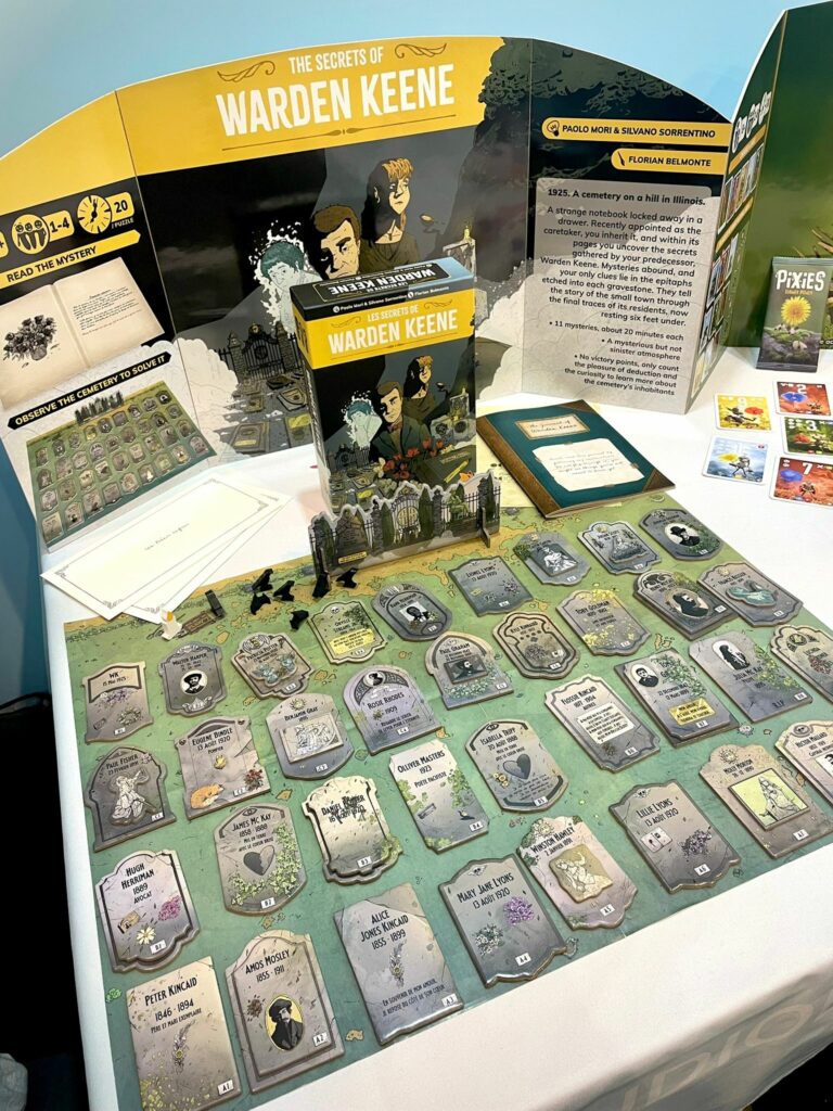 Photo d'un stand de présentation du jeu. On y trouve tout le cimetière avec ses tombes en carton double couche, le carnet de notes, la boite ainsi que les 2 enveloppes qui se trouvent à l'intérieur.