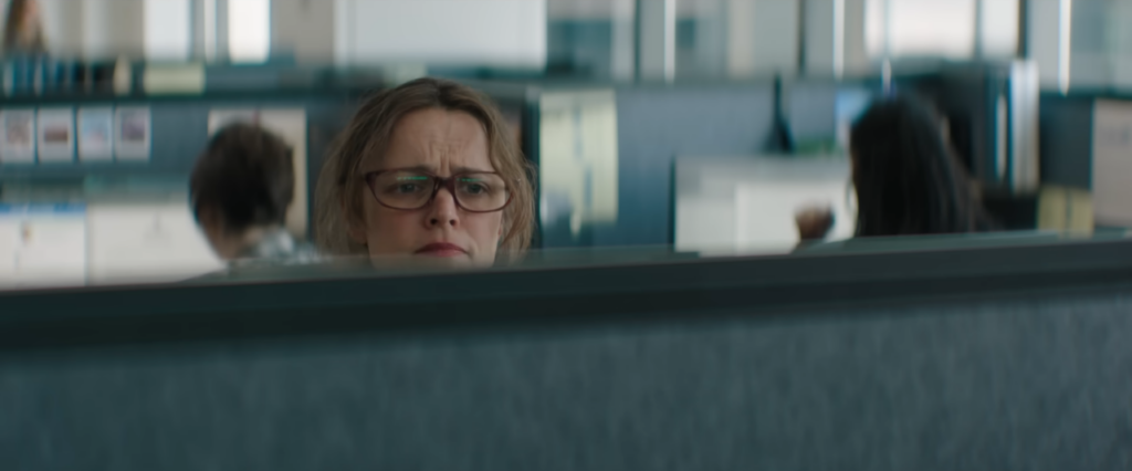 Lydia regarde par dessus le muret du box où elle travaille. Avec de grosses lunettes et des cheveux pas très bien coiffés, elle fronce des sourcils.